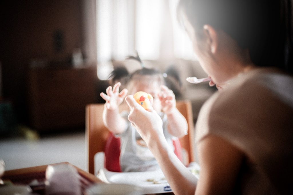 Jeune maman qui donne le repas à son bébé dans une chaise haute