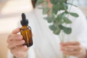 Femme tenant une bouteille d'huile essentielle et une branche de plante verte