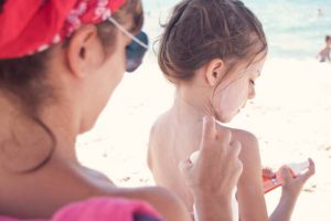 Mère mettant de la crème solaire sur le dos de sa petite fille à la plage