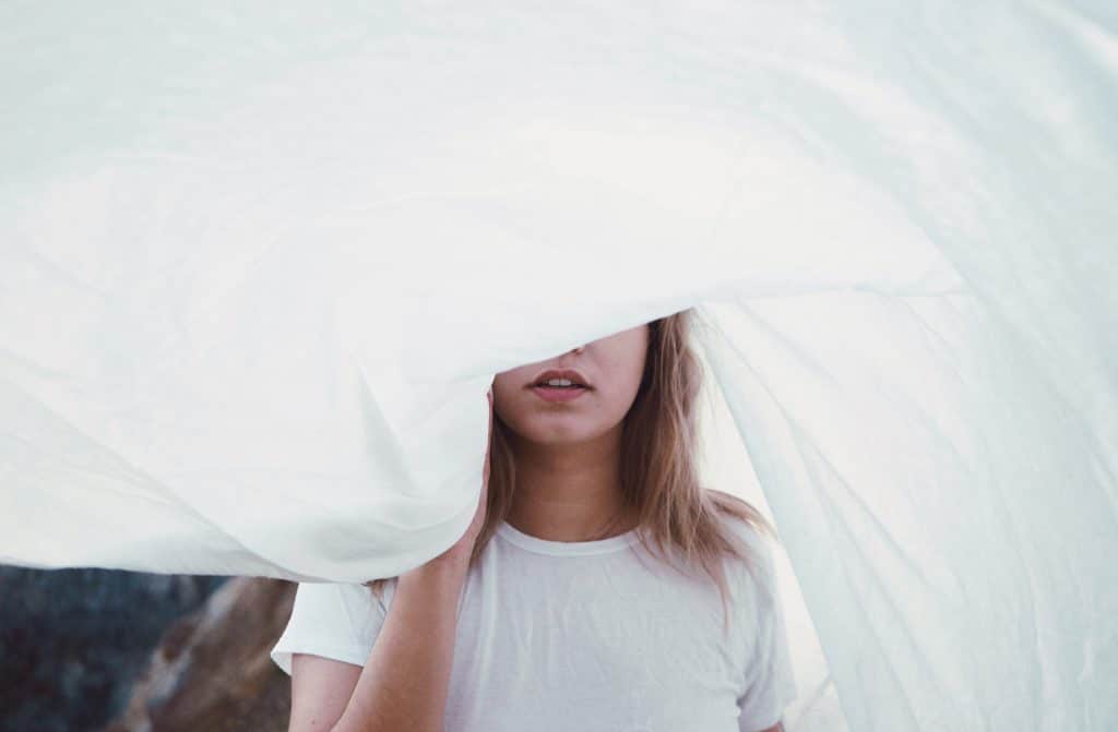 Jeune femme en tshirt blanc qui se cache derrière un drap blanc