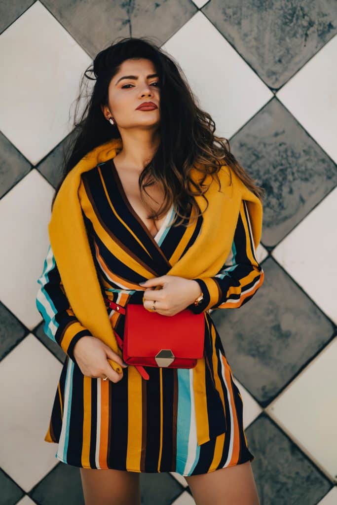 Femme qui porte une robe à rayures verticales jaunes moutarde, bleues et blanches, avec une pochette rouge