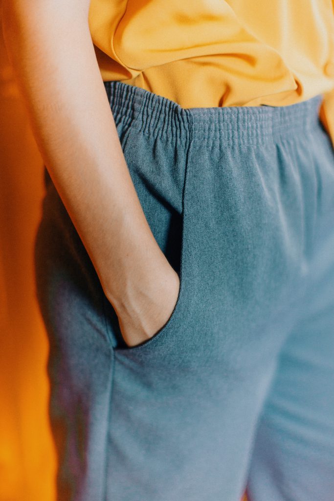 Gros plan sur une femme en jean et tshirt jaune moutarde qui tient sa main dans sa poche