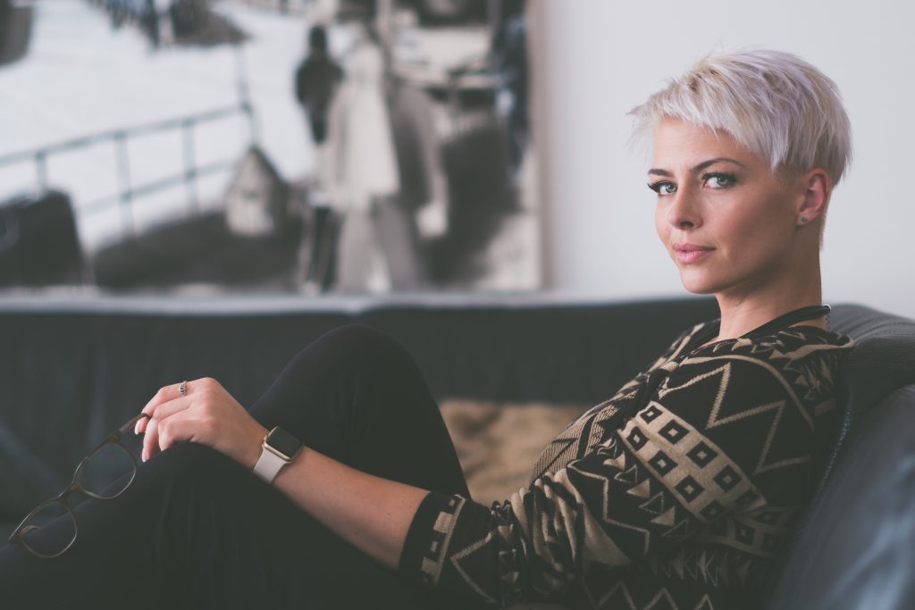 Femme avec les cheveux courts et décolorés, assise sur un canapé