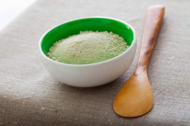 Bol en céramique blanc avec poudre d'argile verte et cuillère en bois