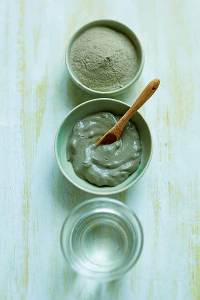 Pots d'eau tiède et d'argile verte utilisés pour la préparation de masques anti boutons sur le visage