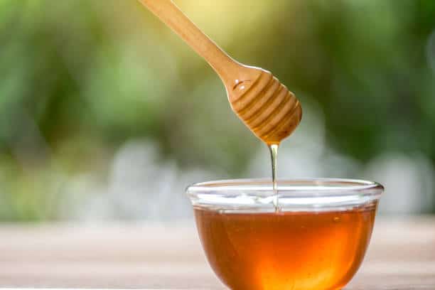 Bol de miel en verre avec cuillère en bois pour préparation masque visage anti boutons miel et argile verte