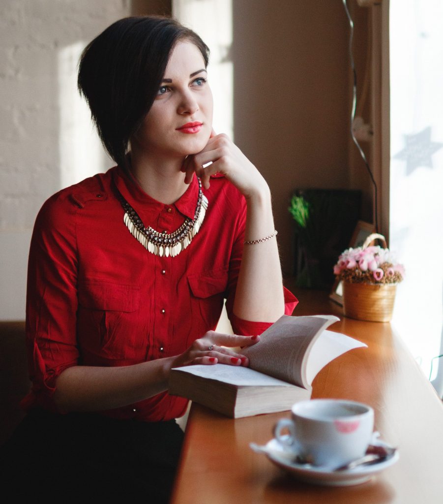 Jeune femme avec haut rouge et collier assise dans un café