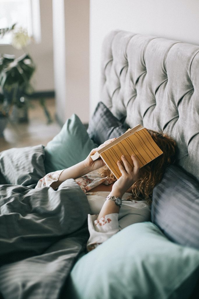 femme dans un lit qui cache son visage derrière un livre