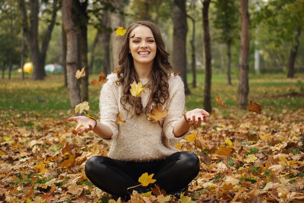 jeune femme souriante assise en tailleur au milieu de feuilles mortes