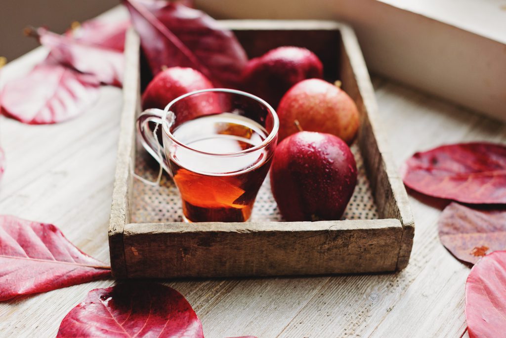 Plateau en bois avec verre de cidre et pommes rouges