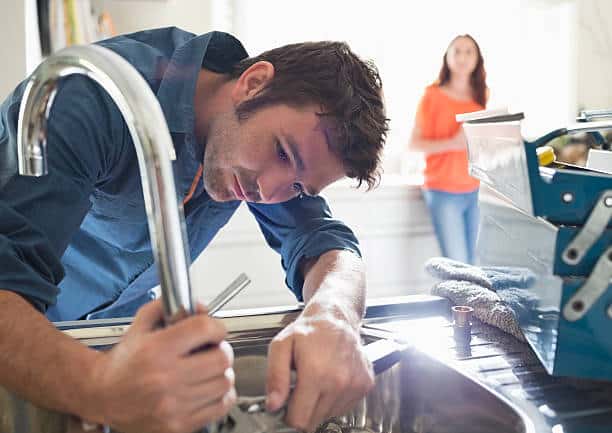 Plombier qui répare le robinet dans l'appartement d'une jeune femme