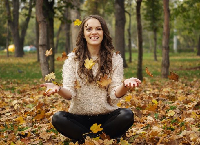 jeune femme souriante assise en tailleur au milieu de feuilles mortes