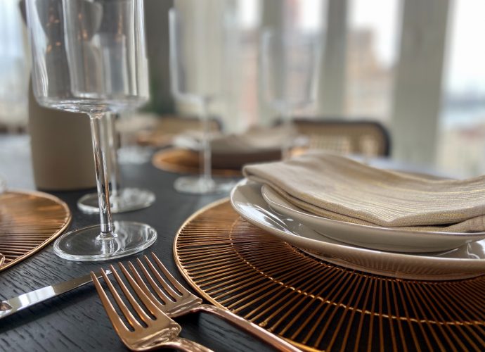 Table dressée avec des assiettes beiges, des verres à vin et des fouchettes dorées